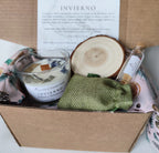 Caja de regalo artesanal que incluye una vela de soja Invierno, una rodaja de madera decorativa, un saquito de tela verde y cerillas en frasco de cristal sobre papel de seda ilustrado